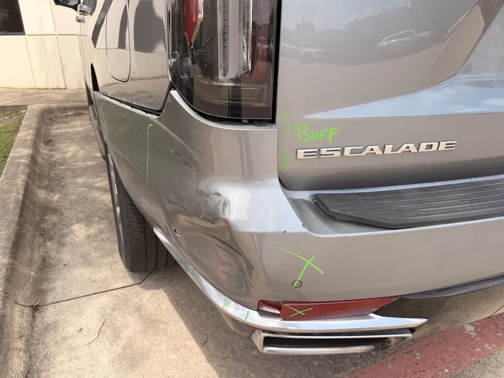 Silver Cadillac Escalade with the rear-left quarter panel and bumper crushed inward and the tail lamp damaged, marked up by an estimator on intake