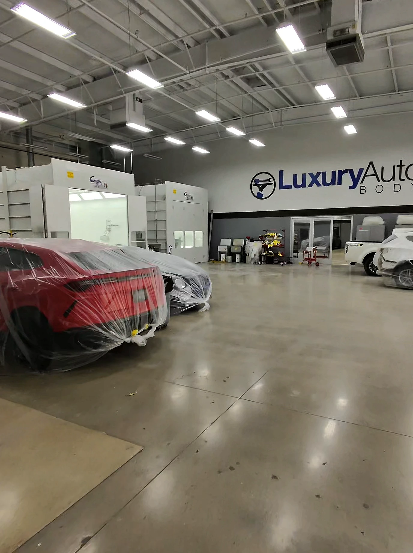 Inside Luxury Auto Body — twin downdraft paint booths beneath the shop sign, vehicles in work