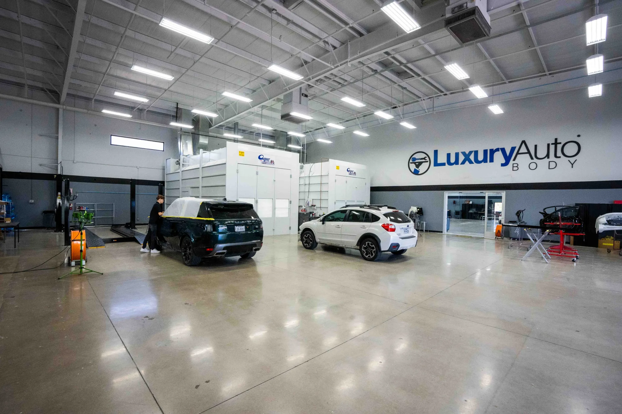 Inside Luxury Auto Body's shop — twin paint booths beneath the Luxury Auto Body sign, vehicles in work