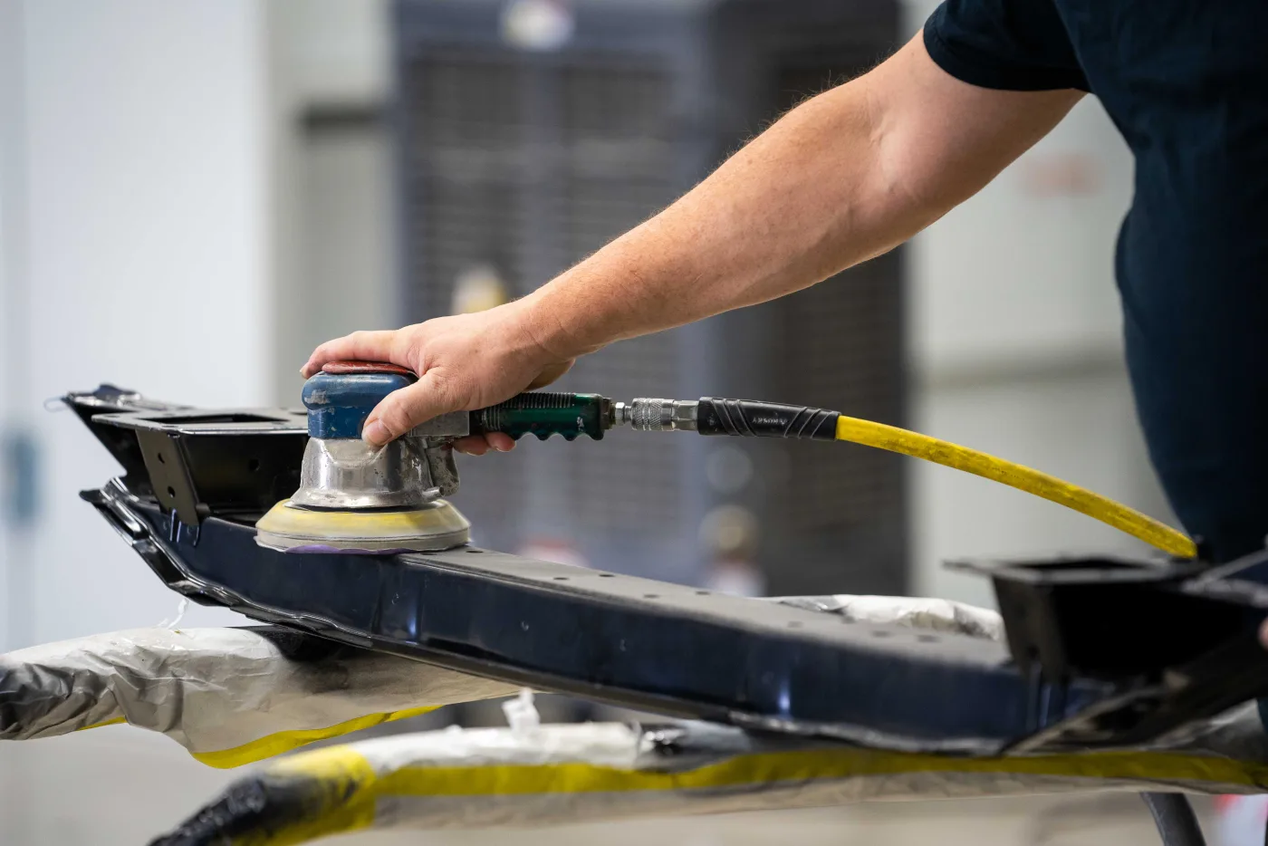 A technician sanding a bumper reinforcement during prep at Luxury Auto Body
