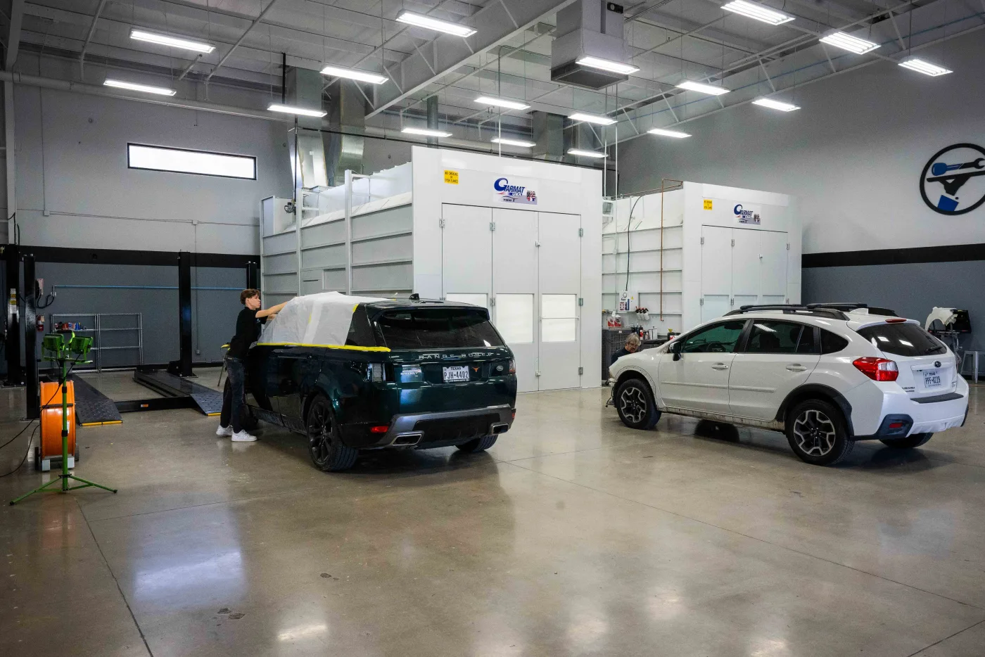 A technician masking a vehicle for refinishing beside the paint booths