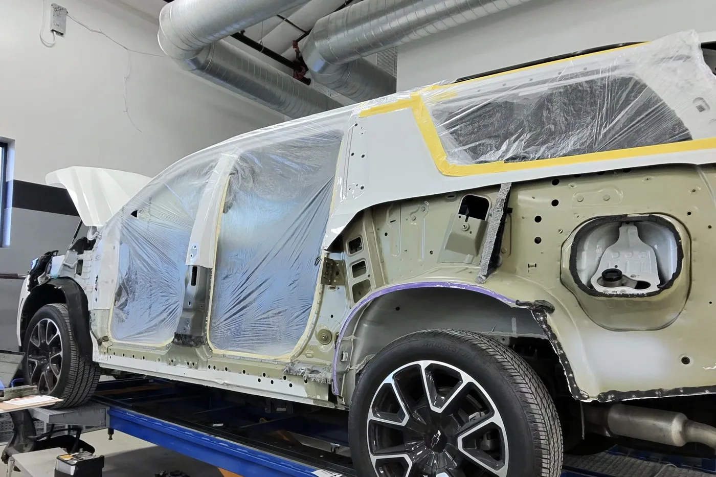 A vehicle stripped and masked on the lift, prepped for refinishing